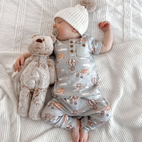 Baby in a patterned onesie holding a teddy bear on a white textured blanket