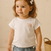 Young girl wearing a white t-shirt with a floral design and blue jeans against a beige background