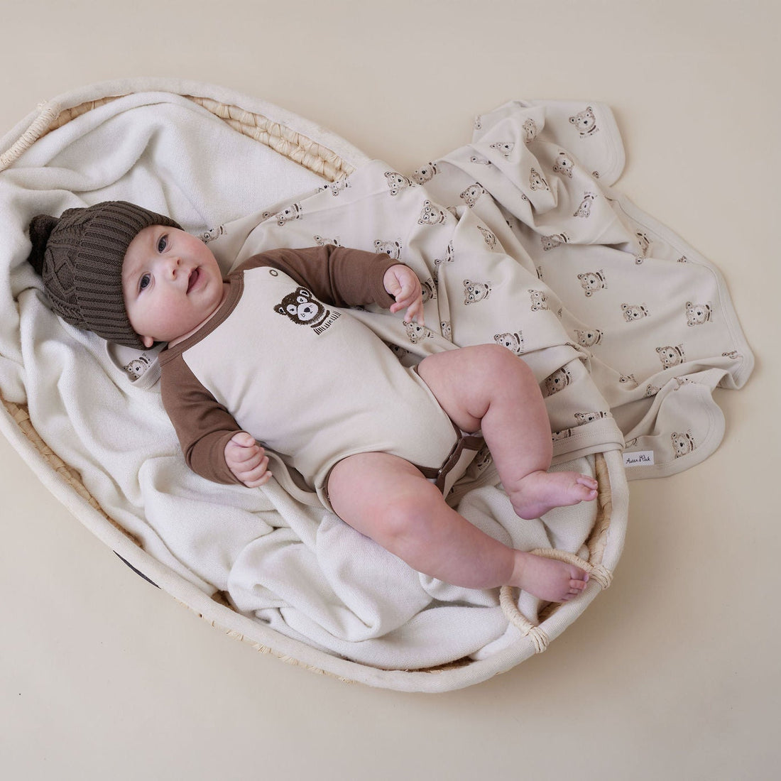 Baby lying in a woven basket with white blanket and brown hat