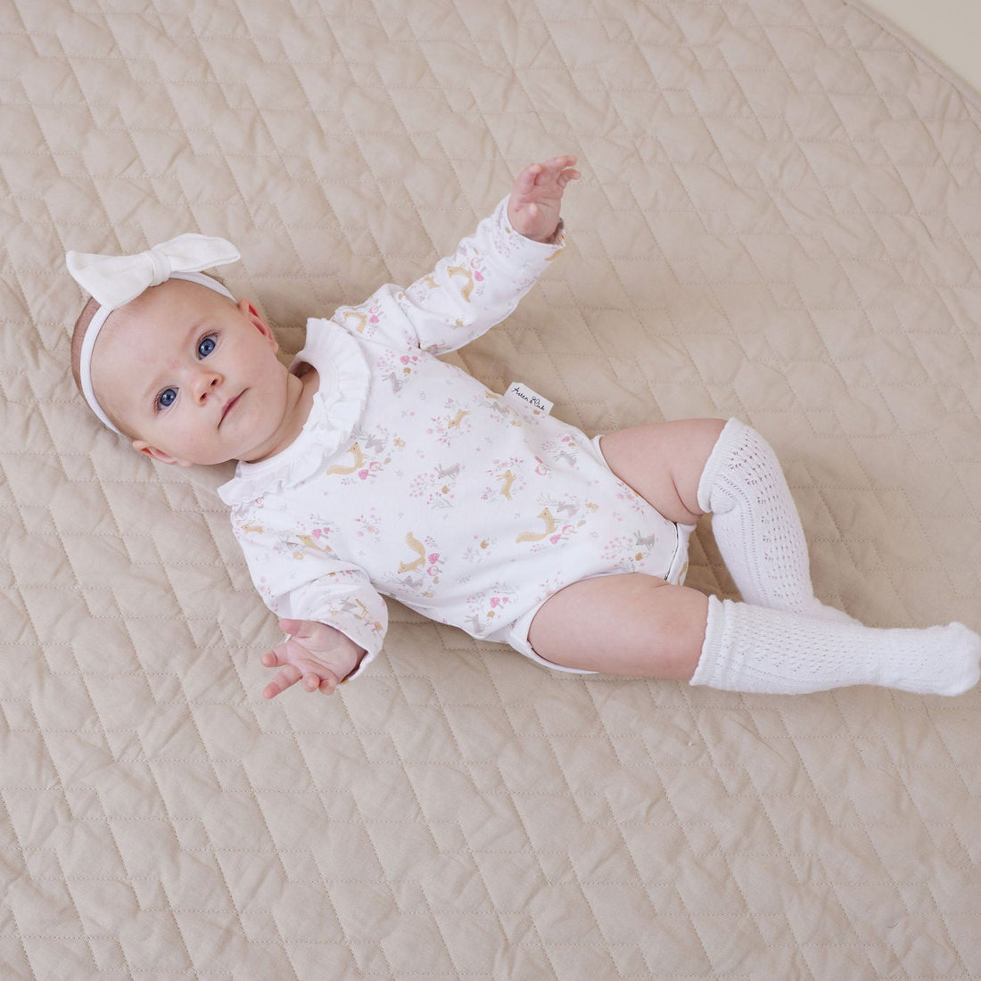 Baby lying on a quilted play mat wearing a white outfit with star patterns.