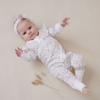 Baby in a white textured outfit lying on a beige surface