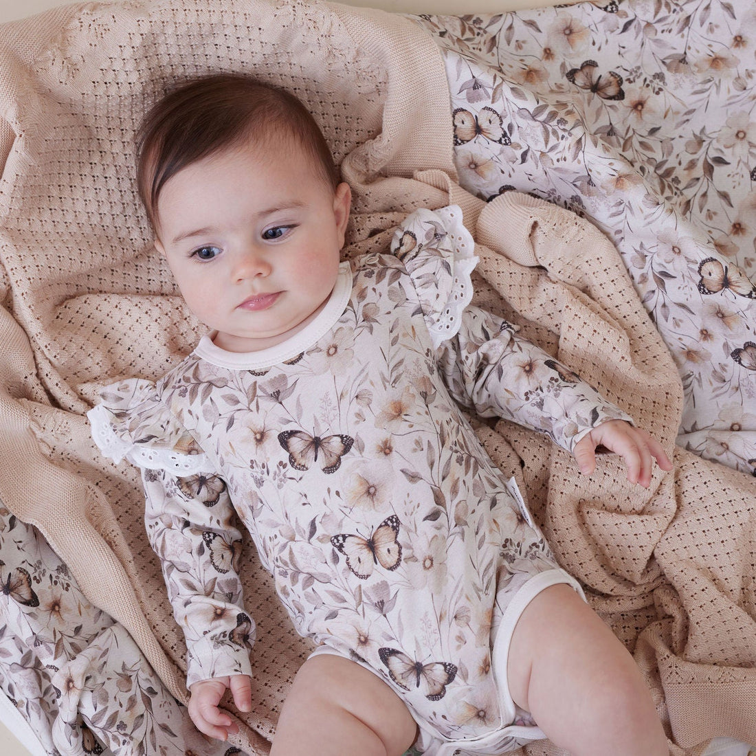 Baby in a floral outfit lying on a textured blanket