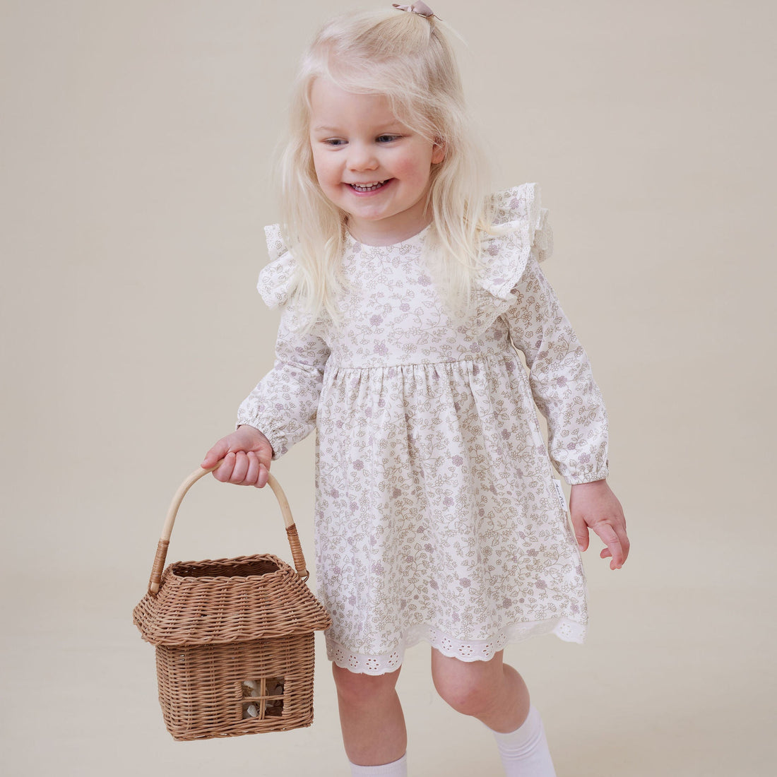 Young girl in a white floral dress holding a wicker basket on a beige background