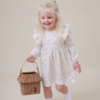 Young girl in a white floral dress holding a wicker basket on a beige background