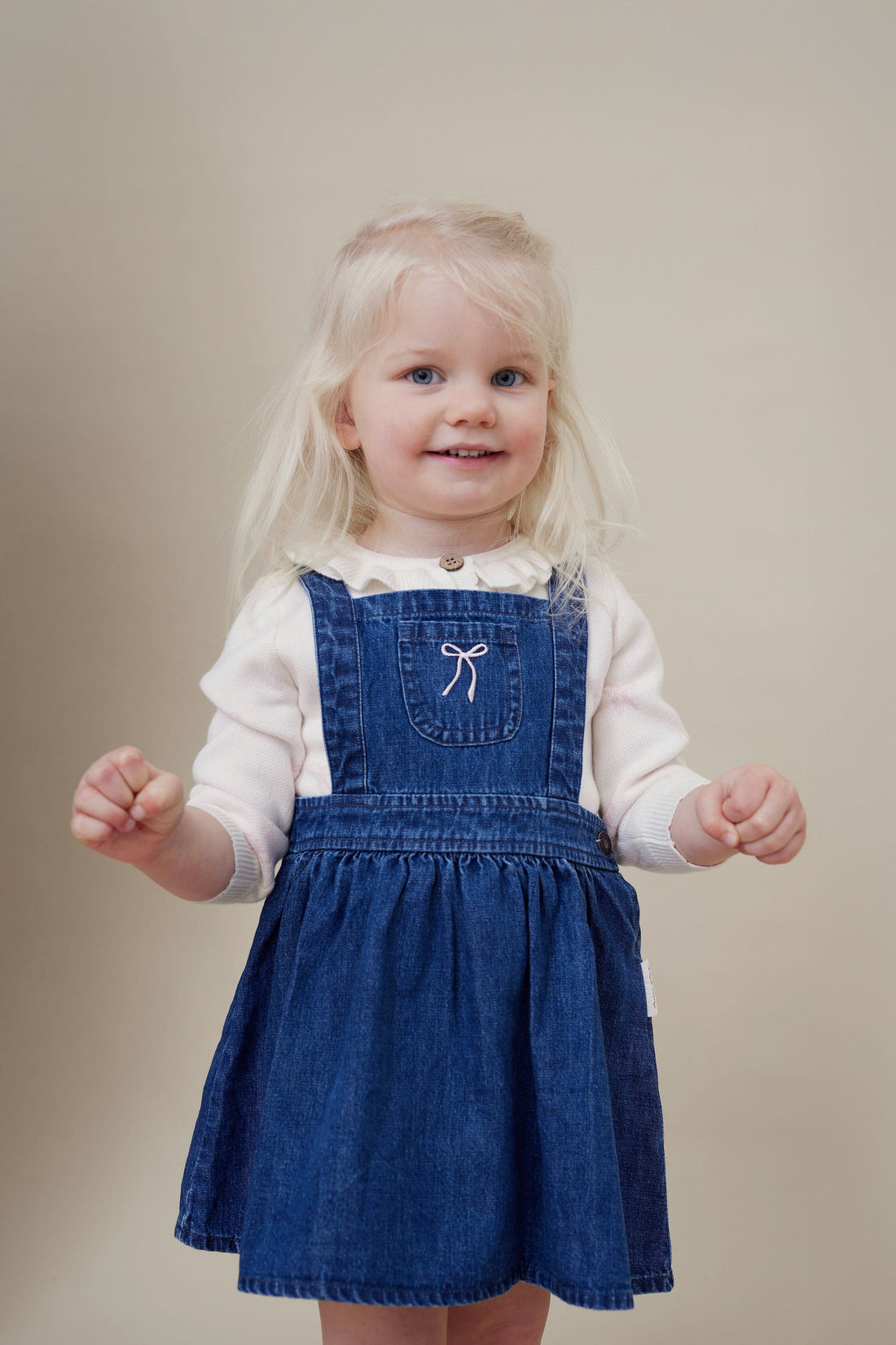 Young girl wearing a blue denim dress with a white bow on a beige background