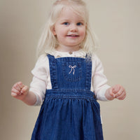 Young girl wearing a blue denim dress with a white bow on a beige background