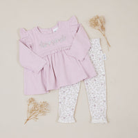 Pink baby top and white patterned leggings on a beige background