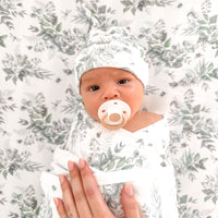 Newborn baby wrapped in a floral patterned blanket with a pacifier and headband.