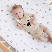 Baby in a bear-themed outfit lying on a crib with a patterned sheet