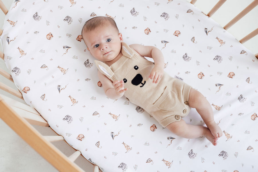 Baby in a bear-themed outfit lying on a crib with a patterned sheet