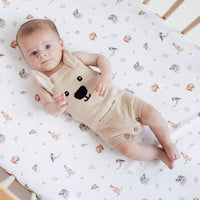 Baby in a bear-themed outfit lying on a crib with a patterned sheet