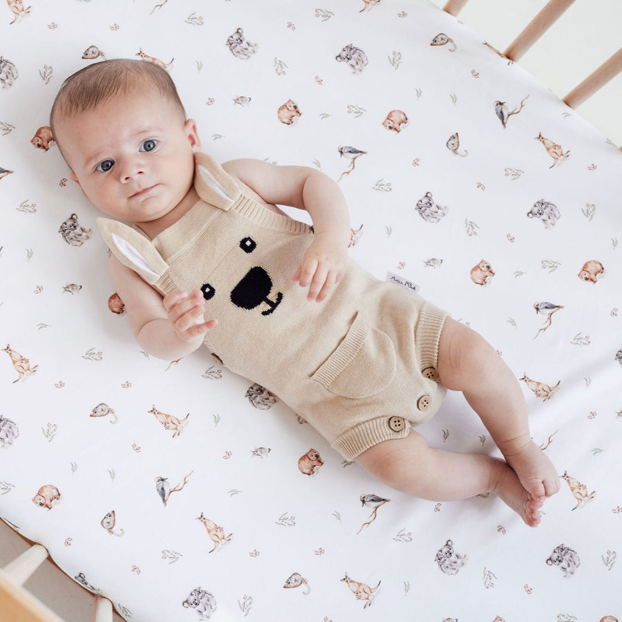 Baby in a bear-themed outfit lying on a crib with a patterned sheet