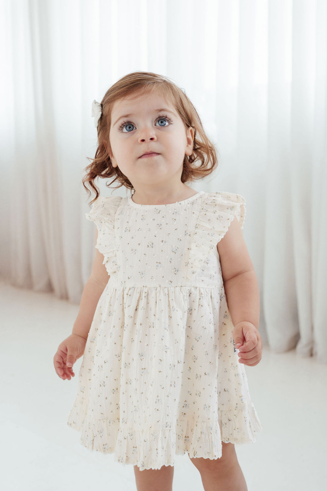 Young girl wearing a white lace dress against a white curtain background