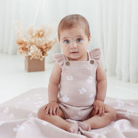Baby wearing a pink floral romper sitting on a white blanket with a light background